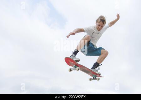 Jeune skateur tendu en saut en hauteur contre le ciel Banque D'Images