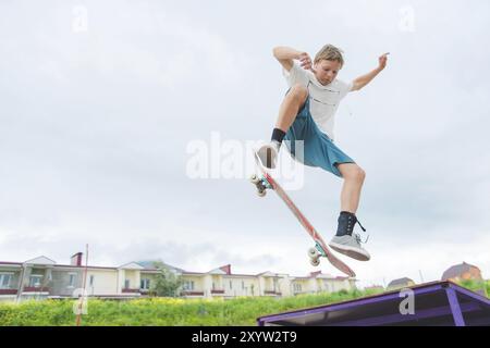 Jeune skateboarder intense en saut en hauteur contre le ciel et les zones de couchage Banque D'Images