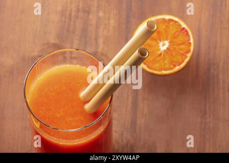 Un gros plan de pailles de bambou réutilisables dans un verre de jus d'orange vibrant. Mise au point sélective Banque D'Images