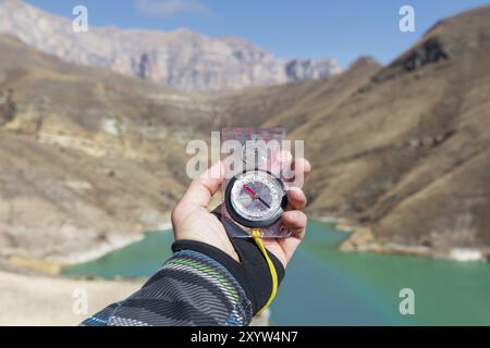 La main d'un homme tient une boussole magnétique de poche pour la navigation sur la toile de fond d'une pente rocheuse et d'un lac de montagne. Le concept de trouver un moyen. G Banque D'Images