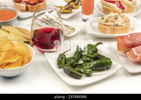 Des tapas espagnols. Un verre de vin rouge avec pimientos del padron poivrons, ensaladilla rusa, gaspacho, salade de jambon, sardines, etc., sur un fond blanc Banque D'Images