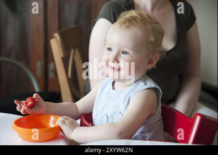 Une petite fille est assise à table et mange des fraises Banque D'Images