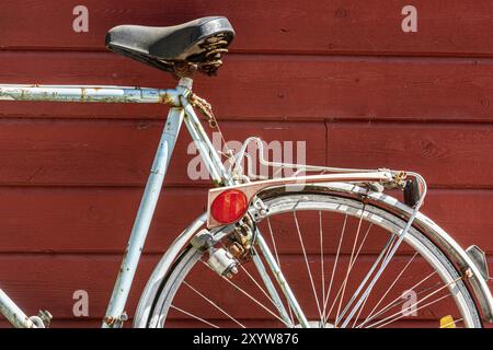 Un vieux vélo bleu et rouillé appuyé contre un mur rouge en bois Banque D'Images