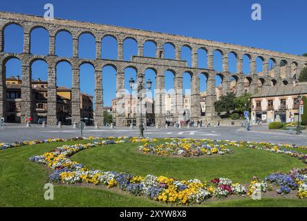 Un aqueduc de pierre historique avec des arches enjambe une ville sous un ciel bleu vif à côté d'un parterre de fleurs coloré, aqueduc, Ségovie, Castilla y Leon, Léon, SP Banque D'Images