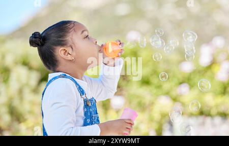 Enfant, fille et bulles soufflant en plein air pour le jeu sensoriel, le développement de l'enfance et l'activité amusante dans la nature. Enfant, jouet en plastique et jeu avec liberté Banque D'Images