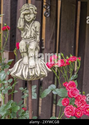 Une figure d'un enfant sur un piédestal, entouré de roses rouges, se tient devant une clôture de piquet en bois dans le jardin, borken, muensterland, allemagne Banque D'Images