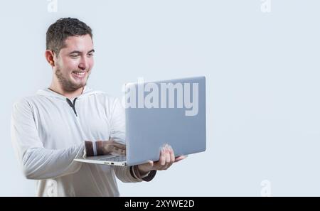 Gars excité tenant et regardant une promotion sur l'écran d'ordinateur portable. Portrait de jeune homme heureux debout à l'aide d'un ordinateur portable isolé Banque D'Images