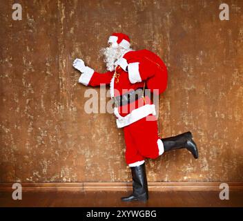 Le Père Noël à marcher avec le grand sac rouge de la présente sur le fond brun Banque D'Images