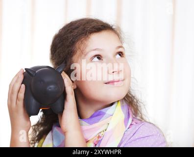 Petite fille économisant de l'argent dans une tirelire. Portrait en intérieur Banque D'Images