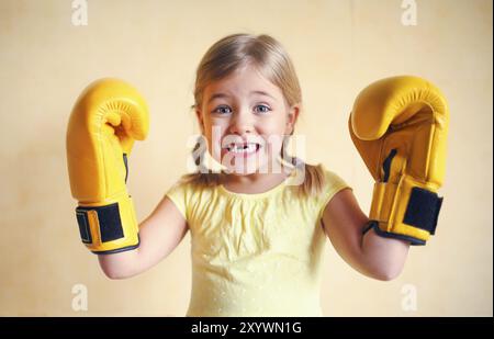 Petite fille aux gants de boxe jaune sur jaune wall background. Girl power concept. Funny little kid portrait. Heureux dent perdue petite fille portrai Banque D'Images