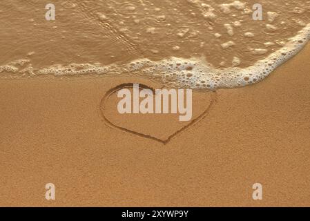 Dessin de coeur dans le sable et vague sur la plage du matin Banque D'Images