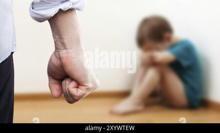 Concept de violence familiale et d'agression, furieux homme en colère leva le poing de punition pour enfant garçon effrayé ou terrifié assis au coin du mur Banque D'Images