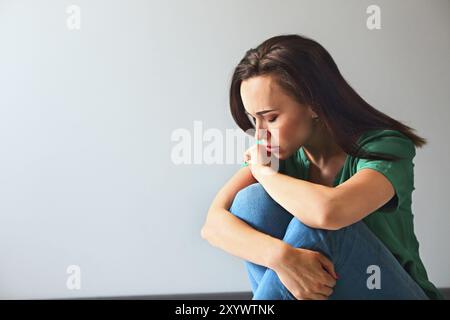 Portrait d'une femme triste à réfléchir sur ses problèmes devant un mur gris Banque D'Images