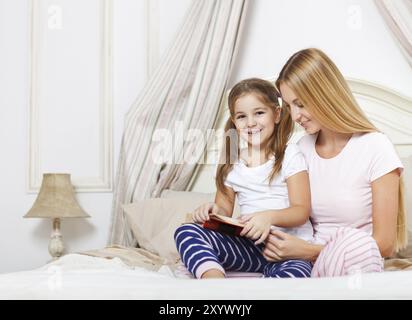 Mère lecture histoire de temps de lit livre à sa fille au lit Banque D'Images