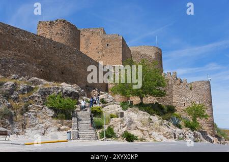 Château historique avec des murs de pierre massifs et des tours, entouré d'arbres et de rochers sous un ciel bleu clair, Consuegra, Tolède, Castille-la Manche, Spai Banque D'Images