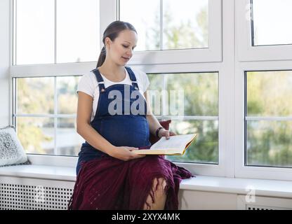 Accueil Portrait de femme enceinte près de la fenêtre de lecture Banque D'Images