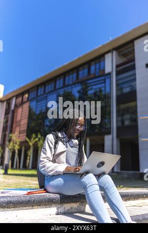 Photo verticale d'une jeune étudiante africaine utilisant un ordinateur portable assis à l'extérieur du campus Banque D'Images