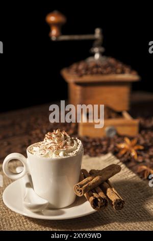 Tasse de café avec de la crème chantilly et le cacao en poudre et moulin café on background Banque D'Images