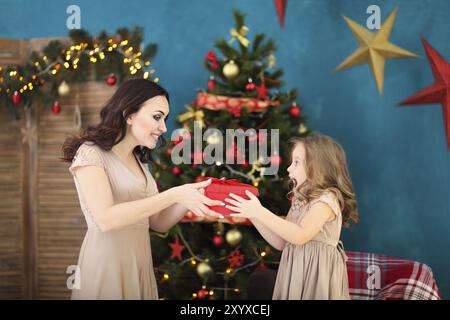 Belle mère heureuse avec sa fille petits sur l'arrière-plan d'intérieur de Noël ensemble et smiling holding present Banque D'Images