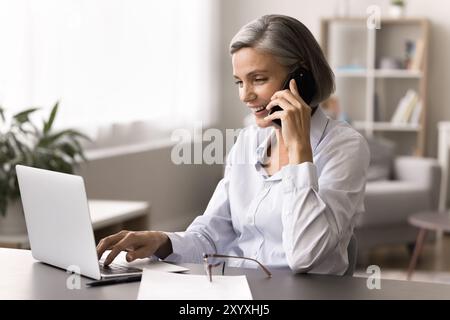 Femme s'engageant dans la conversation au téléphone tout en travaillant sur ordinateur portable Banque D'Images