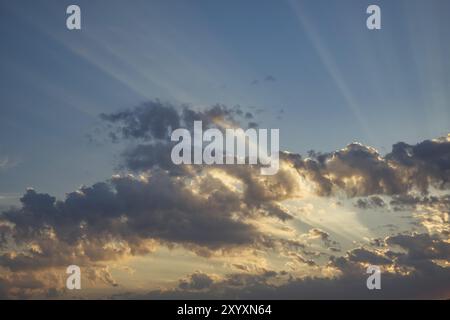 Le ciel est illuminé d'une teinte or-orange, alors que le soleil est à travers les nuages. Les rayons de lumière brillent à travers le cumulus blanc et gris Banque D'Images