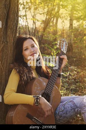 Belle brunette girl joueur de guitare dans la forêt Banque D'Images