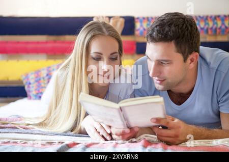 Couple lisant un livre couché dans le même lit Banque D'Images