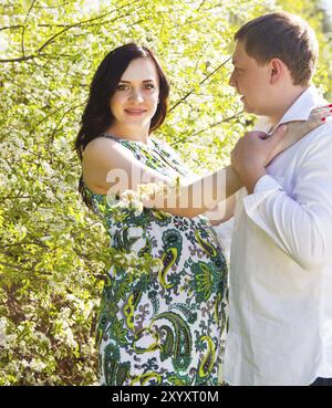 Young happy pregnant couple dans le parc printemps floraison. Portrait en extérieur Banque D'Images