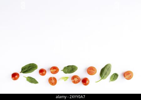 Pose à plat avec des tomates cerises rouges et des feuilles d'épinards vertes sur un fond blanc. Concept d'alimentation saine. Banque D'Images