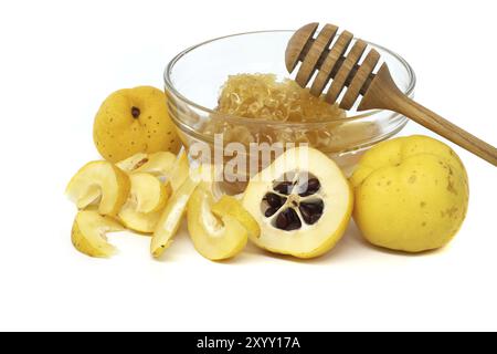 Bol en verre débordant de miel et de godet en bois reposant sur son rebord surmonté de fruits coing vibrants, à la fois tranchés et entiers isolés sur fond blanc Banque D'Images