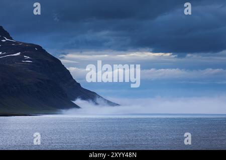 Fjord avec un ciel couvert bleu et de la brume entre deux montagnes sur l'Islande Banque D'Images