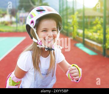 Little smiling girl en patins à roulettes sur l'aire de jeux Banque D'Images