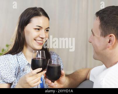 Jeune couple heureux profitant d'un verre de vin rouge à l'intérieur Banque D'Images