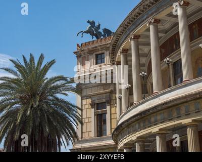 Côté d'un bâtiment historique avec des colonnes et des statues de bronze sur le toit à côté d'un palmier, palerme, sicile, mer méditerranée, italie Banque D'Images