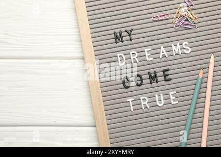 Tableau aux lettres avec phrase My Dreams Come True, crayons et trombones sur table en bois blanc, vue de dessus Banque D'Images