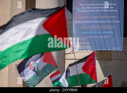 Manchester, Royaume-Uni. 31 août 2024. Drapeaux palestiniens devant une bannière célébrant le 60e anniversaire de la libération de la ville de Manchester par les gardes Grenadiers. Manifestants palestiniens à Manchester lors de leur 48ème week-end de protestation suite à l'attaque du Hamas le 7 octobre. Les manifestants ont défilé dans le centre de Manchester en commençant et en terminant à St Peter's Square. La marche s’est arrêtée au bâtiment d’assurance Axa, sur King Street, pour marquer leurs remerciements pour le désinvestissement de la société en Israël. Des bus et des tramways ont été retenus alors que la marche se déroulait sous escorte policière. Manchester Royaume-Uni. Banque D'Images