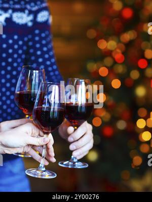 Clinking verres de vin rouge dans les mains sur fond de lumières de Noël. Concept de fête de Noël Banque D'Images