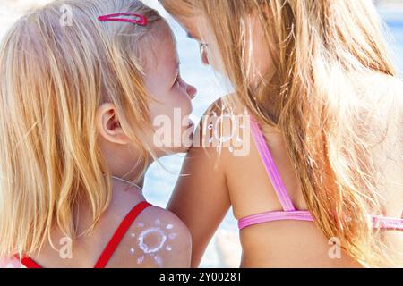 Portrait des sœurs de filles blondes heureuses avec de la crème sur les sholders en forme de rire de soleil et câlin au coucher du soleil. Vacances en famille et soleil protec Banque D'Images