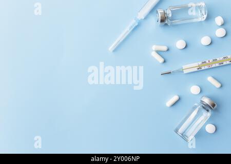 Traitement médicamenteux, concept vaccinal. Thermomètre, bouteilles de vaccin, injection, seringue, pilules sur fond bleu. Banque D'Images