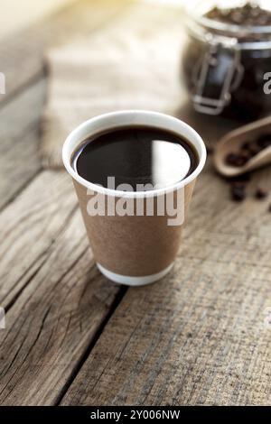 Concept de petit déjeuner au café avec une tasse de papier de café noir expresso, café torréfié sec grains dans le pot en verre et cuillère à l'ancienne table en bois Banque D'Images