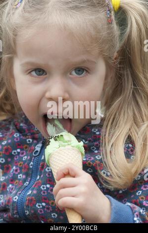 Très mignonne petite fille blonde mangeant de la crème glacée dans une gaufre Banque D'Images