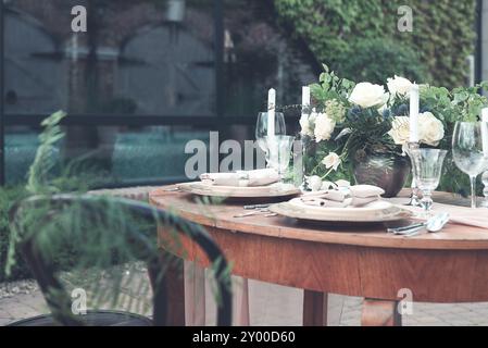 Bougies et vase avec des roses blanches placées sur une table ronde près de verres à vin pendant le mariage dans le jardin Banque D'Images