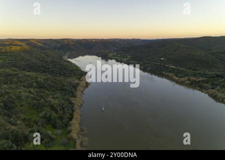 Vue aérienne par drone de Sanlucar de Guadiana en Espagne et d'Alcoutim au Portugal avec bateaux à voile sur le fleuve Guadiana Banque D'Images