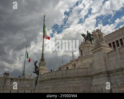 Drapeaux italiens agitant sur un monument avec des sculptures à Rome sous un ciel nuageux, rome, italie Banque D'Images