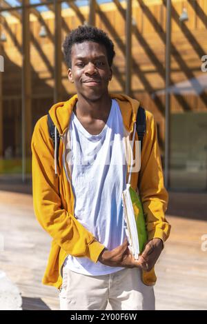 Portrait vertical d'un étudiant africain souriant debout à l'extérieur de l'université sous le soleil Banque D'Images