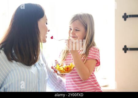 Belle petite fille avec sa mère dans la cuisine manger une salade de fruits frais Banque D'Images