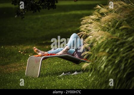 Femme se relaxant sur un transat dans un parc Banque D'Images