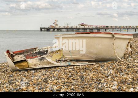 Un bateau cassé sur la plage de galets de Herne Bay, Kent, Angleterre, Royaume-Uni, avec Herne Pier en arrière-plan Banque D'Images