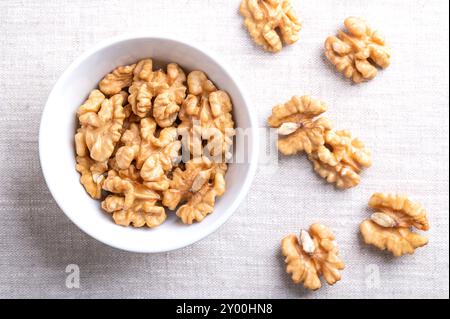 Demi-noyaux de noix dans un bol blanc sur tissu de lin. Moitiés décortiquées et séchées de cerneaux de noix, graines mûres de noyer commun Juglans regia. Banque D'Images