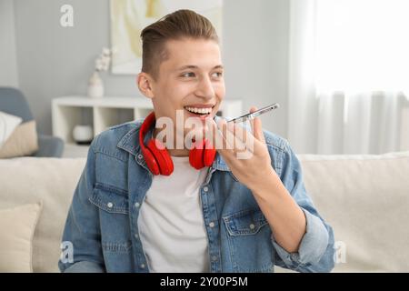 Jeune homme enregistrant un message vocal via smartphone à la maison Banque D'Images